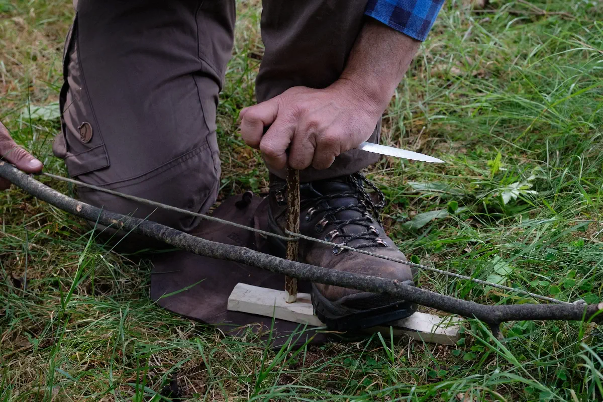 Feuerbohren beim Überlebenstraining mit Messer für die Wildnis